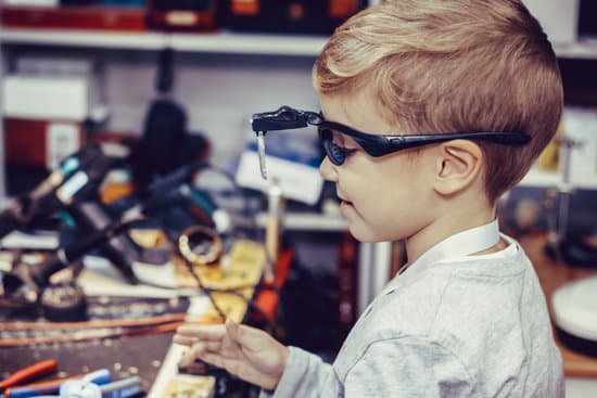 Side view of happy kid with magnifying eyeglasses in engineering workshop.