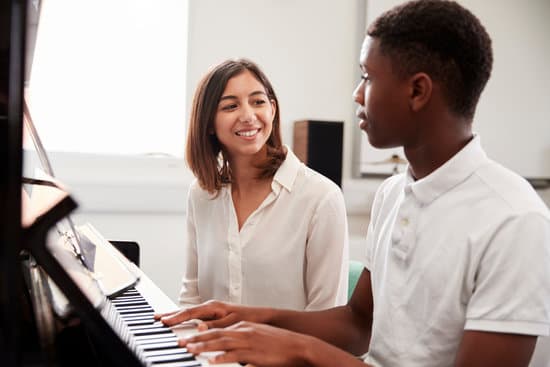 Male Pupil With Teacher Playing Piano In Music Lesson